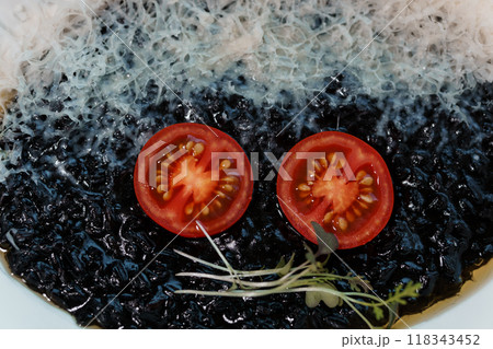 Exquisite Culinary Presentation with Black Risotto, Juicy Tomato Slices, and Delicate Herb Garnish 118343452