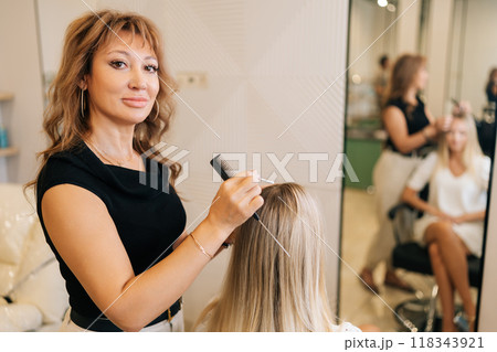 Portrait of woman hairstylist applying peeling purifying and soothing cosmetics product to scalp using cotton swabs. Reflection on mirror of blonde female having professional hair beauty treatment. 118343921