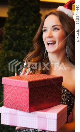 Girl holding Christmas present near New Year tree. Happiness emotions 118344440