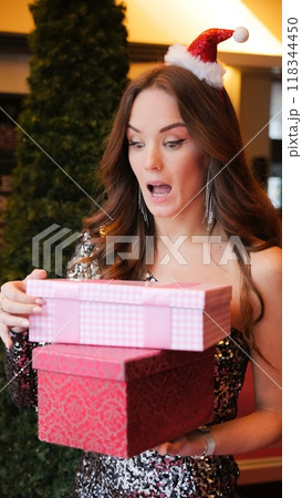 Girl holding Christmas present near New Year tree. Happiness emotions 118344450