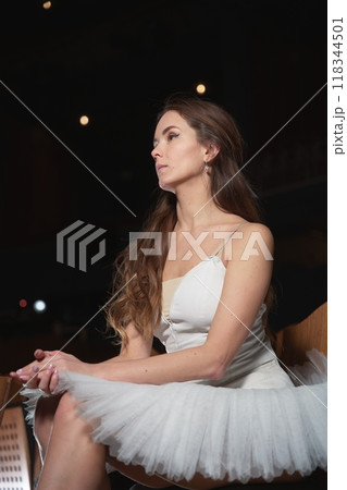 A ballerina in a white tutu and pointe shoes sits on a chair A ballerina in a white tutu and pointe shoes sits on a chair 118344501