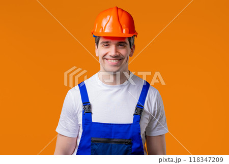 Friendly handyman smiling portrait on orange studio. Positive builder man,helmet Friendly handyman smiling portrait on orange studio. Positive builder man,helmet 118347209