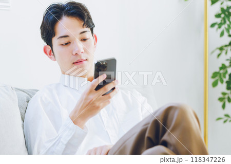 リビングでスマホを見る若い男性 118347226