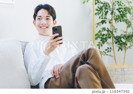 リビングでスマホを見る若い男性 118347392