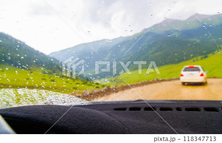 white car driving down the dirt road at rainy summer day in mountains, selective focus view from drivers perspective white car driving down the dirt road at rainy summer day in mountains, selective focus view from drivers perspective 118347713