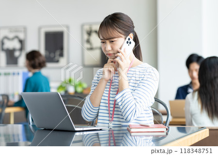 オフィスで電話する若いビジネスウーマン オフィスで電話する若いビジネスウーマン 118348751