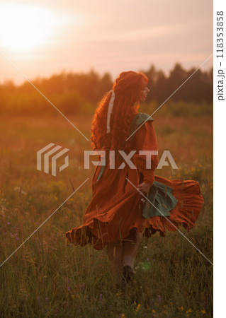 A shepherdess woman with red hair and a green dress sits in a field of flowers. A shepherdess woman with red hair and a green dress sits in a field of flowers. 118353858