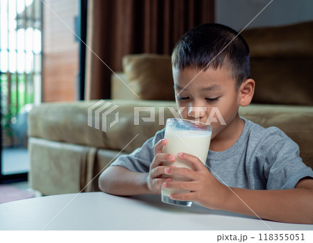 Portrait of a little young handsome kid boy in pink t-shirt, Concept of happy good nutrition, Holding a glass of milk on grey background, Smiling of Asian boy with a glass of milk. 118355051