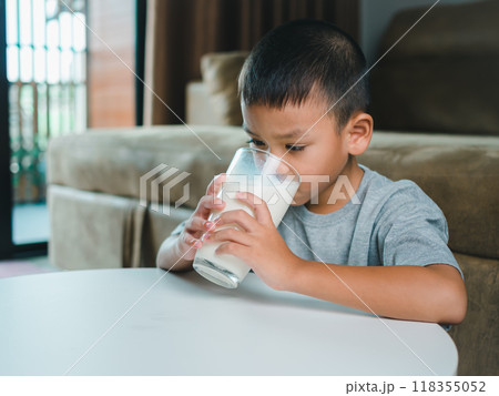Portrait of a little young handsome kid boy in pink t-shirt, Concept of happy good nutrition, Holding a glass of milk on grey background, Smiling of Asian boy with a glass of milk. 118355052