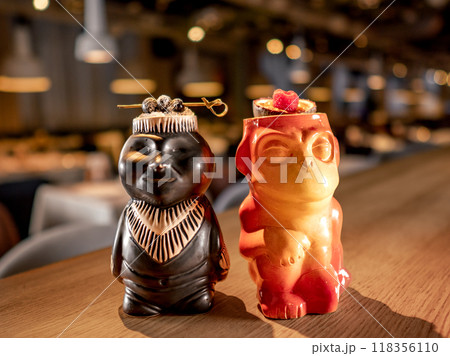 Authentic Tiki Drink Cocktails. Two tropical tiki cocktails on bar counter. Tiki cocktails on bar in night club or restaurant interior 118356110