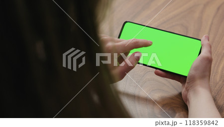 Young woman sitting at a table and using a smartphone with horizontal green screen Young woman sitting at a table and using a smartphone with horizontal green screen 118359842