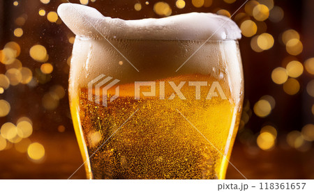 ビールの白い泡がグラスから溢れそうになっている。金色のボケの背景。 118361657