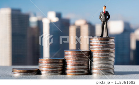 積み上げられたコインの上に立つビジネスマンのミニチュアフィギュア。ビジネスでの収入の上昇のイメージ。 118361682