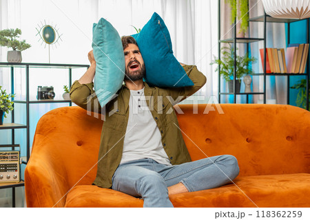 Neighbors repair work, irritated man by loud music at home cover ears with pillows annoyed by noise 118362259