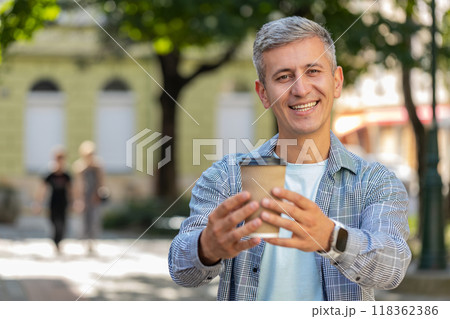 Happy mature Caucasian man enjoying drinking morning coffee hot drink and smiling on city street Happy mature Caucasian man enjoying drinking morning coffee hot drink and smiling on city street 118362386