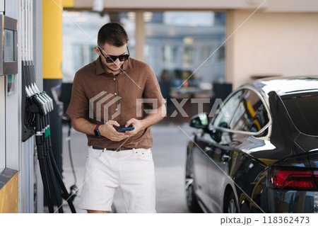 Handsome stylish man check petrol prices in another petrol station. Fuel price increase. Luxury car Handsome stylish man check petrol prices in another petrol station. Fuel price increase. Luxury car 118362473