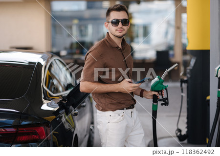 Handsome man in sunglasses hold green fuel pump in hand. Starting refueling car. Benzine Handsome man in sunglasses hold green fuel pump in hand. Starting refueling car. Benzine 118362492