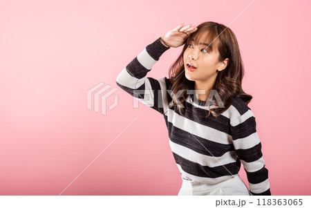 Searching concept. Asian woman looking far away with hand over head at studio shot isolated on pink background, Portrait of Happy female looking at distance with eyes shaded, copy space 118363065
