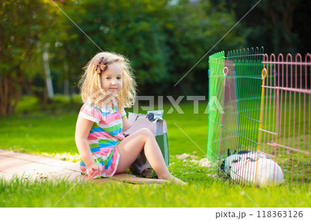 Kids feed rabbit in sunny garden 118363126
