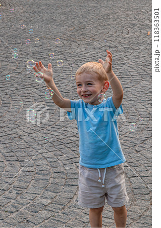 Little joyful boy catches soap bubbles on the street 118363501