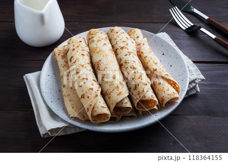 Thin pancakes rolled into a roll on a plate. The concept of a delicious breakfast or Maslenitsa. wooden background. Thin pancakes rolled into a roll on a plate. The concept of a delicious breakfast or Maslenitsa. wooden background. 118364155