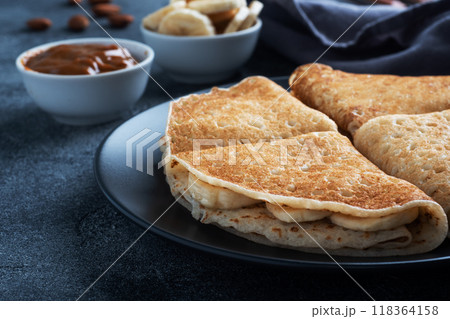 Pancakes with chocolate banana filling. Delicious breakfast of pancakes envelopes on a plate, dark concrete background. Pancakes with chocolate banana filling. Delicious breakfast of pancakes envelopes on a plate, dark concrete background. 118364158