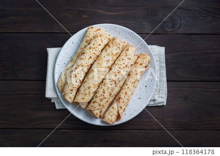 Thin pancakes rolled into a roll on a plate. The concept of a delicious breakfast or Maslenitsa. wooden background. copy space Thin pancakes rolled into a roll on a plate. The concept of a delicious breakfast or Maslenitsa. wooden background. copy space 118364178