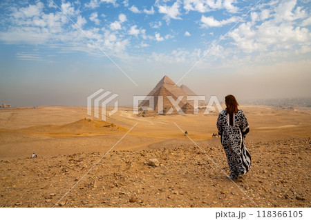 A rear view of a woman in a long traditional Muslim dress looking at the 3 great Pyramids in Egypt A rear view of a woman in a long traditional Muslim dress looking at the 3 great Pyramids in Egypt 118366105
