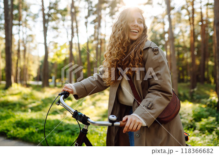 Happy pensive young woman in stylish clothes riding bike in sunny park, outdoors. Active lifestyle. Happy pensive young woman in stylish clothes riding bike in sunny park, outdoors. Active lifestyle. 118366682