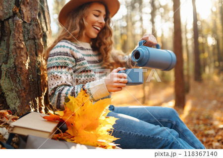 Cute young woman drinks hot drink from thermos and enjoys nature. Autumn landscape. relax concept. 118367140