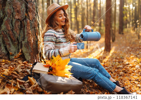 Cute young woman drinks hot drink from thermos and enjoys nature. Autumn landscape. relax concept. 118367141