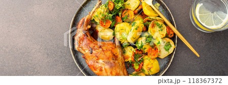 Baked rabbit with potatoes and carrots, a set table with food, a glass of wine and a vase of flowers 118367372