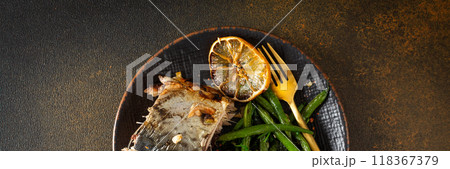 Enjoy a nutritious meal of baked green beans with onions and baked mackerel, beautifully arranged on a plate against a brown background banner 118367379