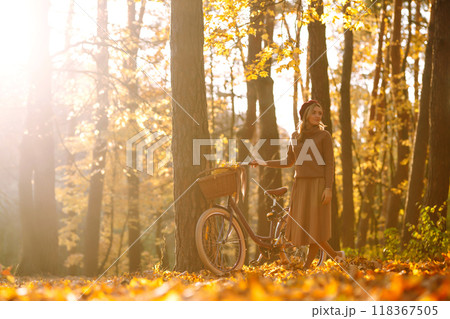 Young smiling woman with a bicycle walks in the autumn forest at sunset. Young smiling woman with a bicycle walks in the autumn forest at sunset. 118367505