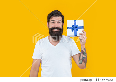 happy bearded guy with present box in studio. guy with present isolated on yellow background. happy bearded guy with present box in studio. guy with present isolated on yellow background. 118367988