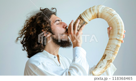 Man with curly hair blowing shofar horn for cultural celebration. Concept of Jewish New Year holiday Rosh Hashanah 118368465