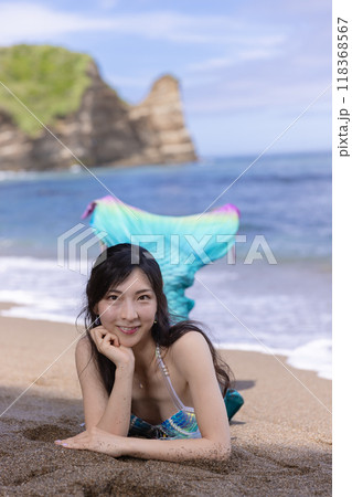 夏の海辺の砂浜に座って微笑む若い女性の人魚 118368567