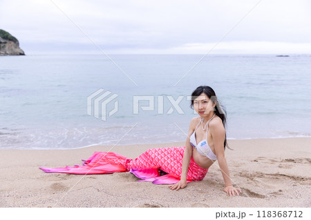 海の砂浜に座りこちらに目線を送る若い女性の人魚 118368712