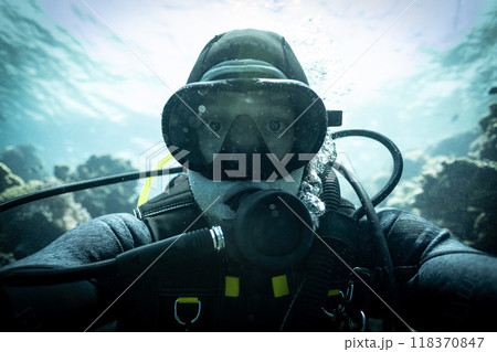 Scuba diver man swimming on a blue water sea looking at camera Scuba diver man swimming on a blue water sea looking at camera 118370847