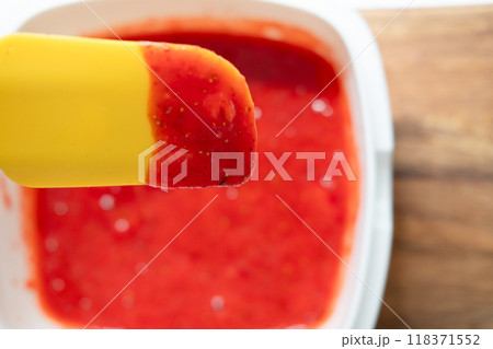 red and liquid strawberry jelly in a container and a yellow spatula for stirring after the blender 118371552