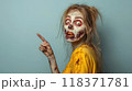 Portrait of living dead woman on background of light blue wall, zombie points finger to side. Theme of scary Halloween, people, showing, shopping, sale, person. 118371781