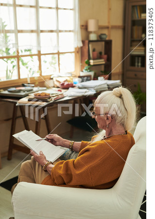 Senior Woman Sitting Indoors Reading Book Peacefully Senior Woman Sitting Indoors Reading Book Peacefully 118373405