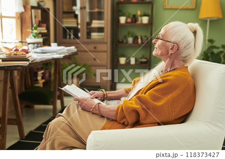 Elderly Woman Reading Book in Cozy Living Room Setting Elderly Woman Reading Book in Cozy Living Room Setting 118373427