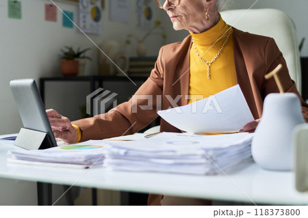 Senior Woman Using Tablet and Holding Documents at Desk Senior Woman Using Tablet and Holding Documents at Desk 118373800