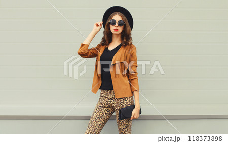 Beautiful stylish young woman posing with handbag in black hat, jacket, glasses on city street 118373898