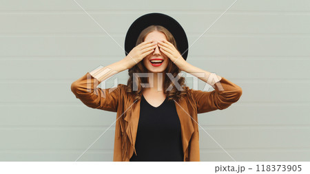 Stylish surprised young woman covering her eyes with hands, fashionable girl in black round hat 118373905