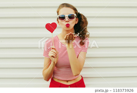 Beautiful young woman with red heart shaped sunglasses blowing kiss on white wall background Beautiful young woman with red heart shaped sunglasses blowing kiss on white wall background 118373926
