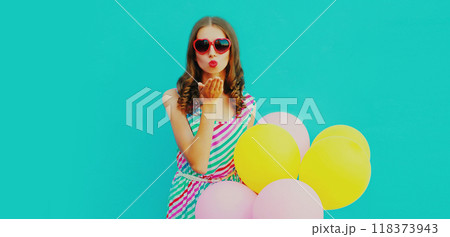 beautiful young woman with bunch of balloons blowing kiss in colorful dress on blue background beautiful young woman with bunch of balloons blowing kiss in colorful dress on blue background 118373943
