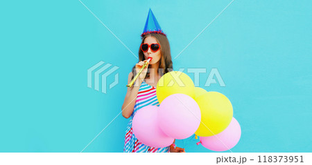 Portrait of cheerful young woman in a birthday cap with colorful balloons on a blue background 118373951