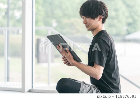 タブレット端末を使うスポーツウェア姿の若いアジア人男性 118376393